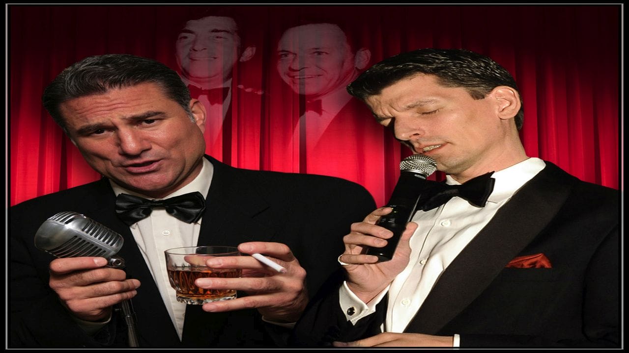 Two men in tuxedos perform on stage with vintage microphones; one holds a glass of whiskey. Red curtains and faint images of two classic performers appear in the background. South Florida Business & Wealth