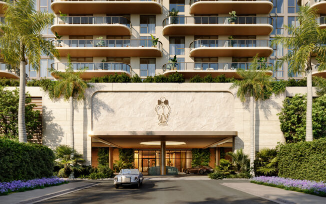 The entrance of a modern luxury hotel features a stone facade, lush greenery, palm trees, and two classic cars parked by the covered driveway, with balconies and plants visible on the upper floors. South Florida Business & Wealth
