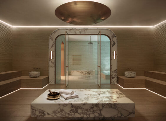 Luxurious marble steam room with a central marble table, folded towels, and a bronze bowl. The space has glass doors, indirect lighting, and minimalist décor, creating a serene and elegant atmosphere. South Florida Business & Wealth