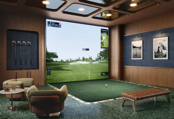 A modern indoor golf simulator room with a large digital screen showing a golf course, a putting mat, golf clubs on the wall, armchairs, a bench, and framed golf photos on blue walls. South Florida Business & Wealth