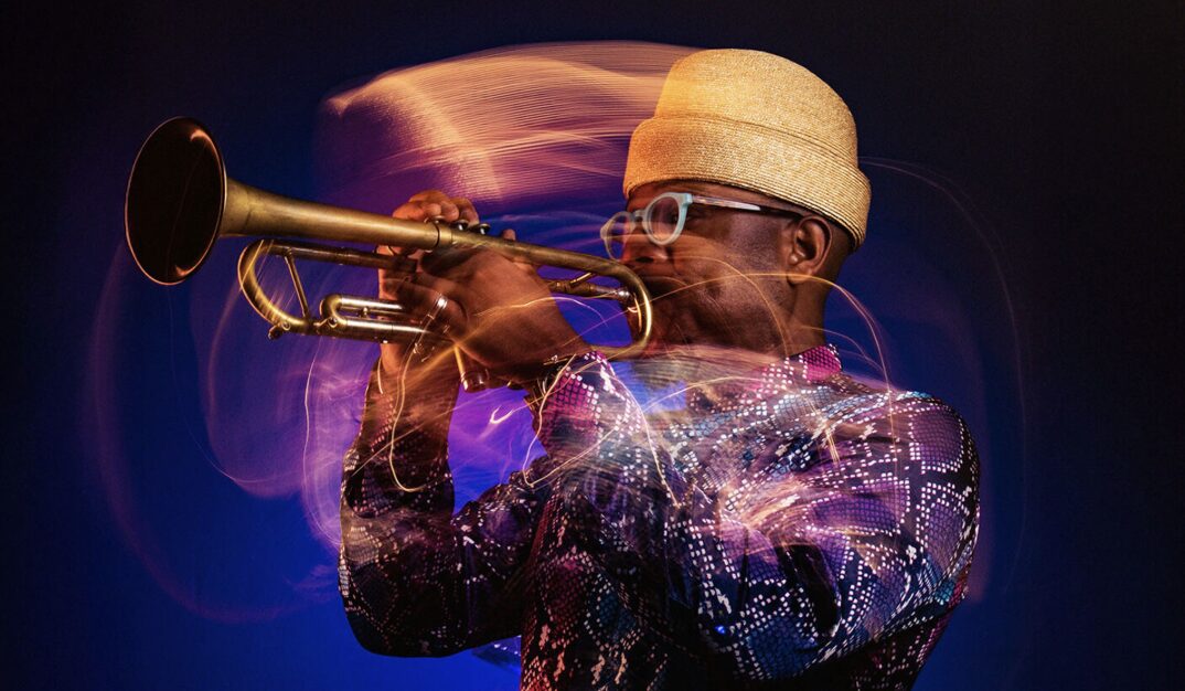 A man wearing glasses and a straw hat plays a trumpet, surrounded by swirling, colorful light trails against a dark background. South Florida Business & Wealth