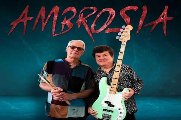 Two men stand in front of a blue background with "AMBROSIA" written in red above them. One holds drumsticks, wearing sunglasses and a patterned shirt; the other holds a green electric bass guitar and wears a black patterned shirt. South Florida Business & Wealth