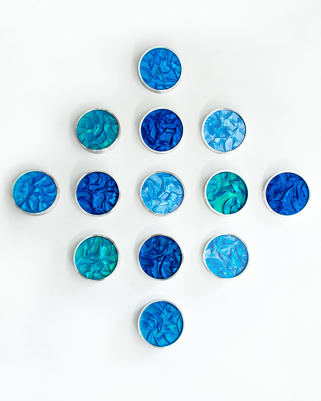 Thirteen round tins with blue and teal marbled surfaces are arranged in a diamond pattern on a white background. South Florida Business & Wealth