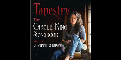 A woman with long brown hair sits by a window in cozy light, wearing a gray sweater and jeans. Text reads: "Tapestry: The Carole King Songbook starring Suzanne O Davis." A cat sits in the lower right corner. South Florida Business & Wealth