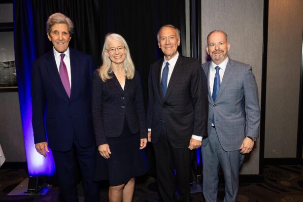 Four professionally dressed people, three men in suits and a woman in a skirt suit, stand side by side indoors in front of a curtain, smiling at the camera. South Florida Business & Wealth