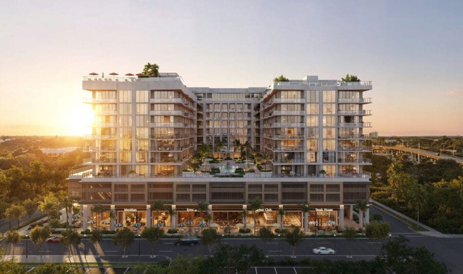 A modern, multi-story building with large glass windows, rooftop greenery, and palm trees at sunset. The lower level features shops facing a street with cars and lush surrounding trees. South Florida Business & Wealth