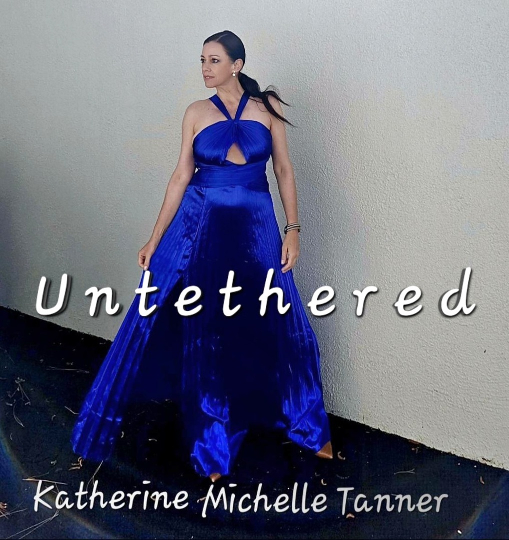 A woman in a flowing, bright blue gown stands against a plain light wall. Text across the image reads "Untethered" and below, "Katherine Michelle Tanner. South Florida Business & Wealth