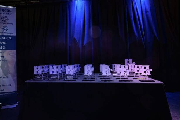 A table covered with numerous glass awards and plaques, set against a dark curtain backdrop with blue stage lighting. South Florida Business & Wealth
