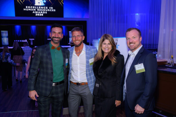 Four people dressed in business attire smile and pose together at an indoor event. A screen in the background reads "Excellence in Human Resources Awards 2026." The room is lit with blue lighting. South Florida Business & Wealth