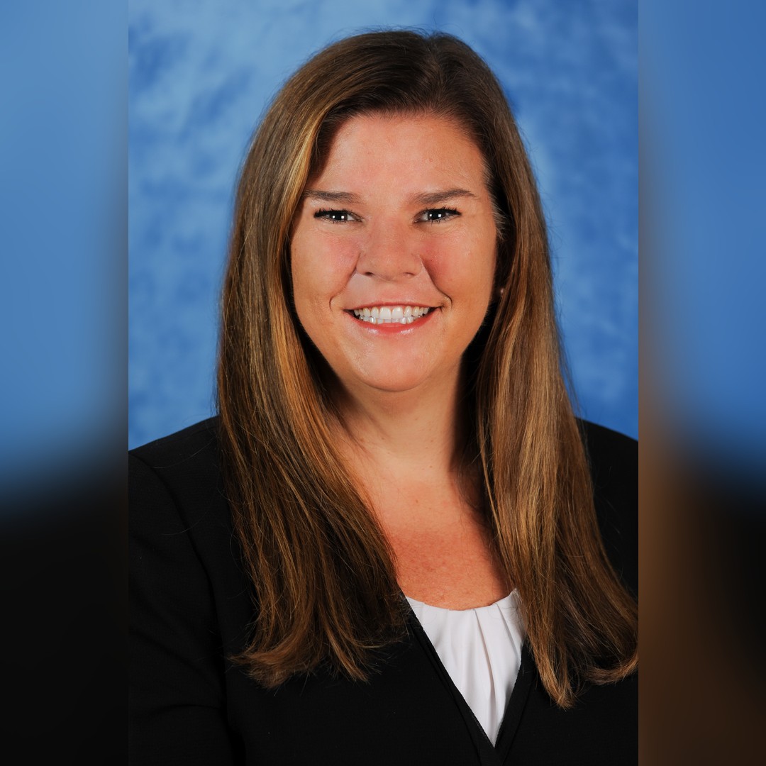 A woman with long brown hair wearing a black blazer and white top smiles at the camera in front of a blue, textured background. South Florida Business & Wealth