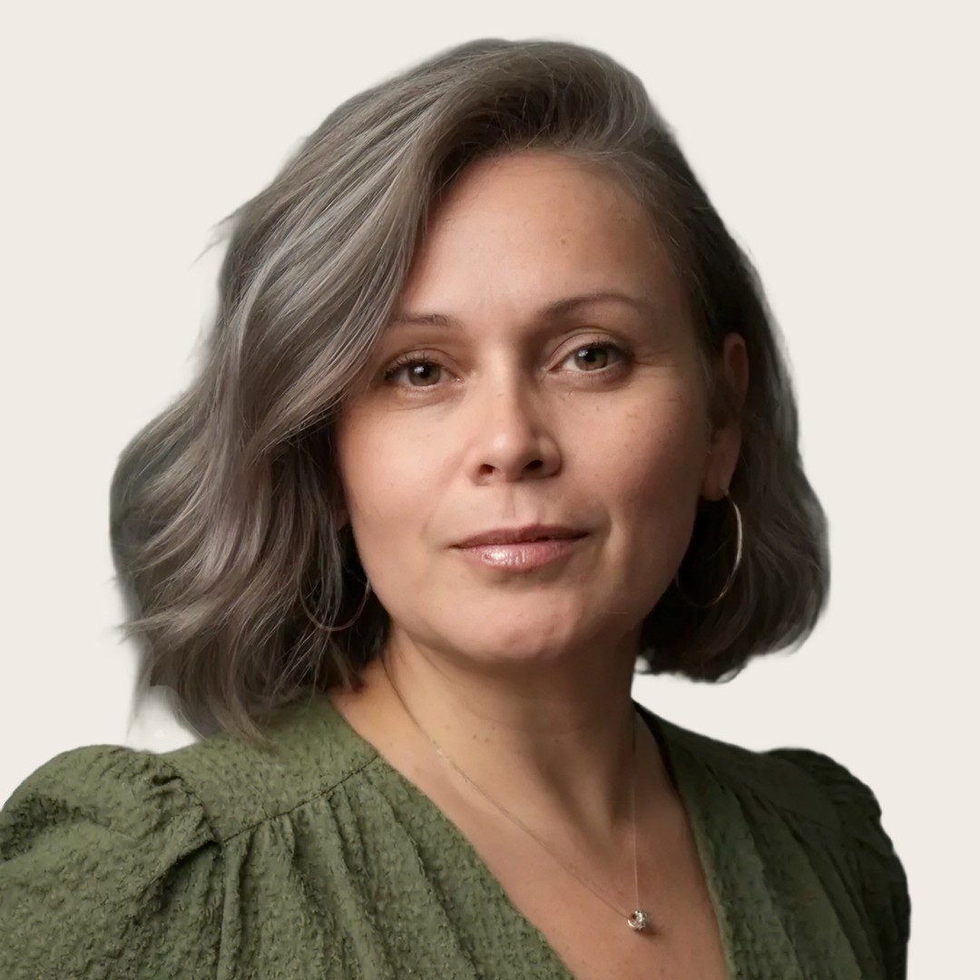 A woman with shoulder-length gray hair wearing a green textured top, gold hoop earrings, and a necklace, looking confidently at the camera against a plain light background. South Florida Business & Wealth