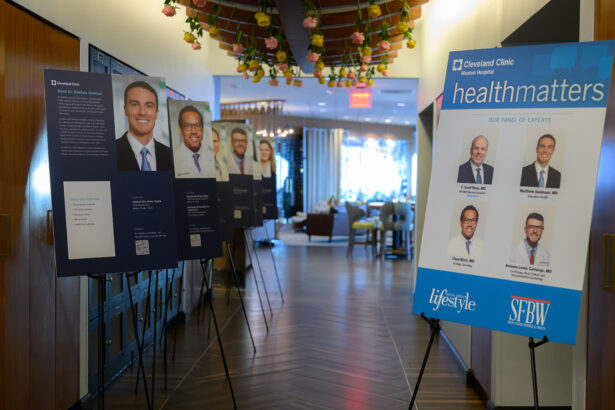 A hallway displays several poster boards on easels featuring portraits and bios of medical professionals. A larger sign reads "healthmatters" with photos of a panel of experts from Cleveland Clinic. The space is brightly lit and decorated. South Florida Business & Wealth