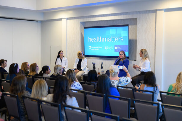 A panel of four women, including two in white coats, speaks to an audience in a conference room. A screen behind them displays "healthmatters" and Cleveland Clinic and Lifestyle logos. South Florida Business & Wealth