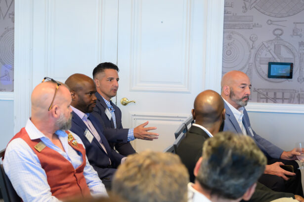 A group of men in business attire sit in a conference room; one man in the center gestures while speaking, engaging with others around him. South Florida Business & Wealth