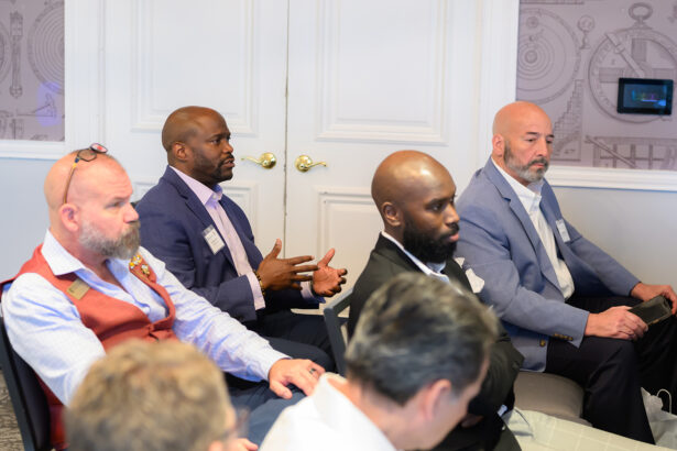 A group of men in business attire sit in a meeting room; one man in a purple shirt is speaking with hands gesturing, while others listen attentively. South Florida Business & Wealth