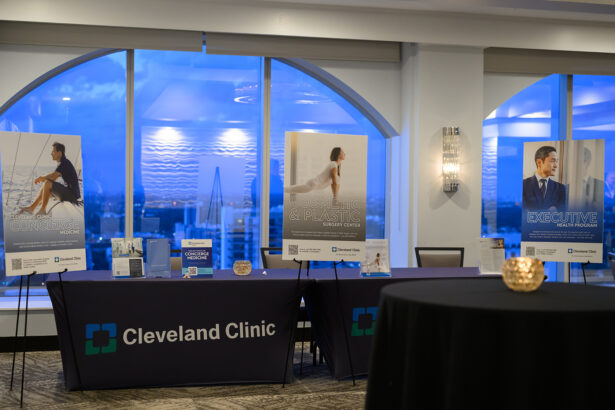 A Cleveland Clinic event booth with three display tables and large posters promoting concierge medicine, cosmetic surgery, and executive health services, set in a modern room with city views through large windows. South Florida Business & Wealth