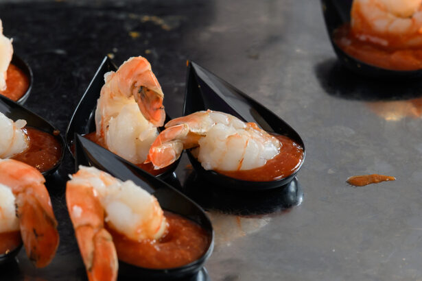 Cooked shrimp are served with cocktail sauce in small black serving spoons, arranged on a reflective surface. South Florida Business & Wealth