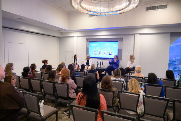 A group of people sits in rows facing a panel of four women speakers on a stage in a conference room. A screen behind them displays “healthmatters” and photos of the panelists. South Florida Business & Wealth