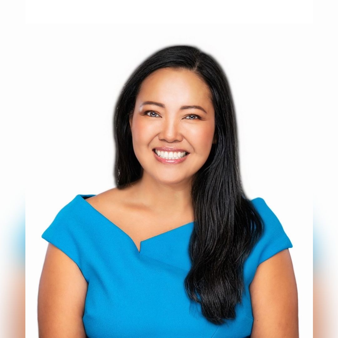 A woman with long black hair and a bright smile, wearing a blue top, is posed against a white background. South Florida Business & Wealth