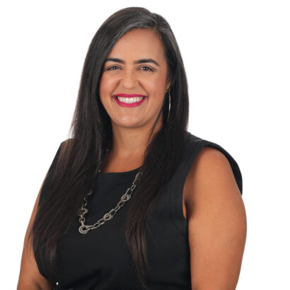 A woman with long, straight dark hair wearing a sleeveless black top and a silver chain necklace smiles against a plain white background. South Florida Business & Wealth