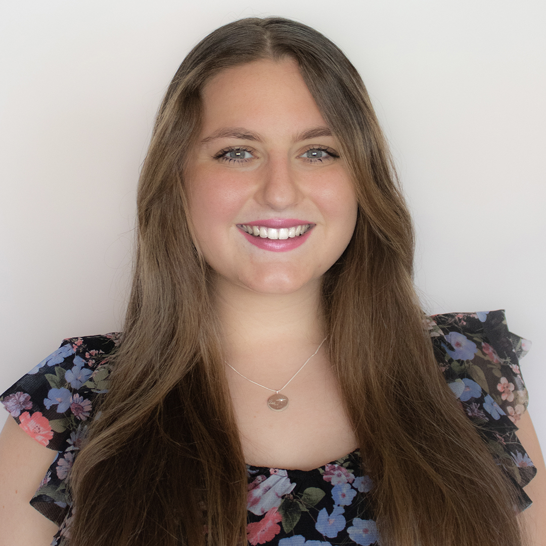 A woman with long brown hair wearing a floral dress and a silver necklace smiles at the camera against a plain light background. South Florida Business & Wealth