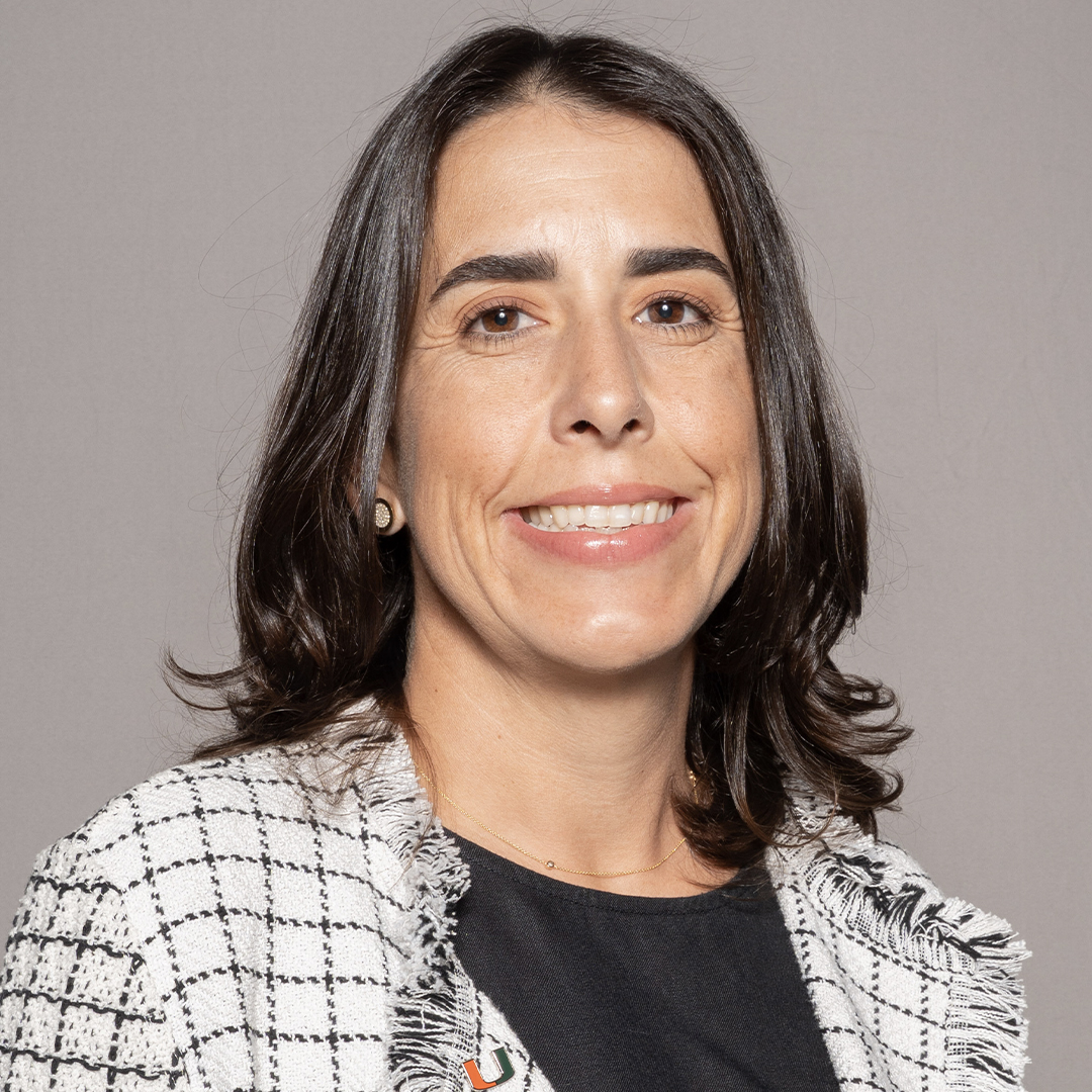 A woman with shoulder-length dark brown hair smiles at the camera. She is wearing a black top and a white checkered blazer, standing against a plain light gray background. South Florida Business & Wealth