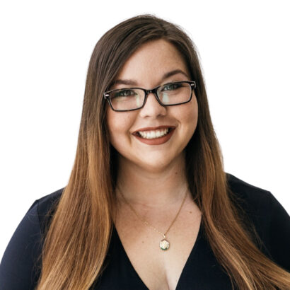 A woman with long brown hair and glasses, wearing a dark top and a pendant necklace, smiling in front of a plain white background. South Florida Business & Wealth