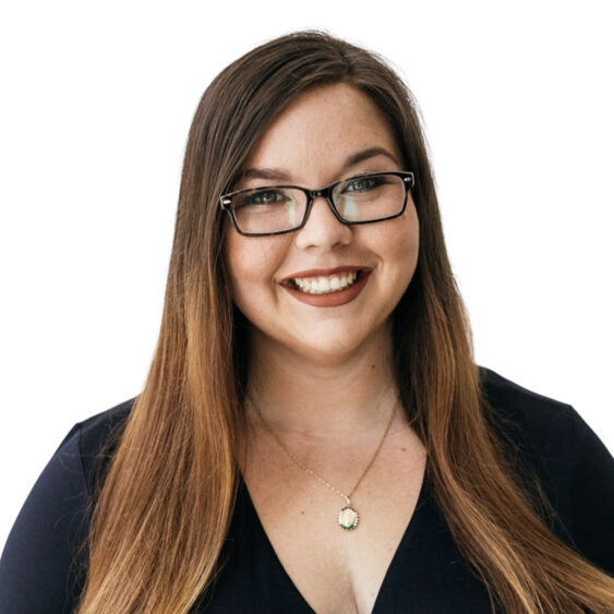 A woman with long brown hair and glasses, wearing a dark top and a pendant necklace, smiling in front of a plain white background. South Florida Business & Wealth
