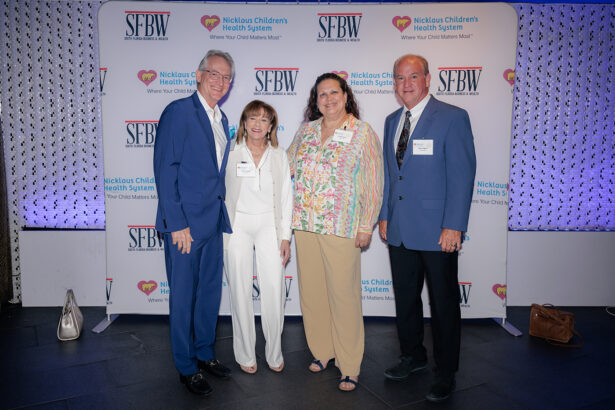 Four adults pose and smile together in front of a step-and-repeat banner with logos for SFBW and Nicklaus Children’s Health System at an indoor event. The group is dressed in business or business-casual attire. South Florida Business & Wealth