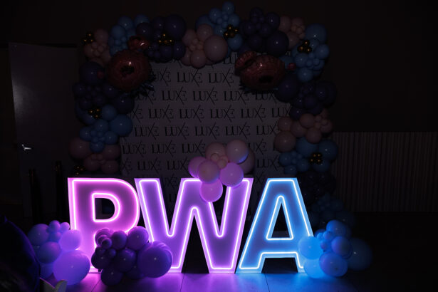 Large illuminated letters "PWA" are decorated with clusters of pink and blue balloons, set in front of a backdrop that repeatedly says "LUXÉ." The display is festive and celebratory. South Florida Business & Wealth