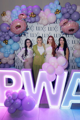 Four women stand in front of a "LUXE" backdrop, surrounded by pink, purple, and blue balloon arrangements. Large illuminated letters spell "PWA" with balloon decorations in front of them. South Florida Business & Wealth