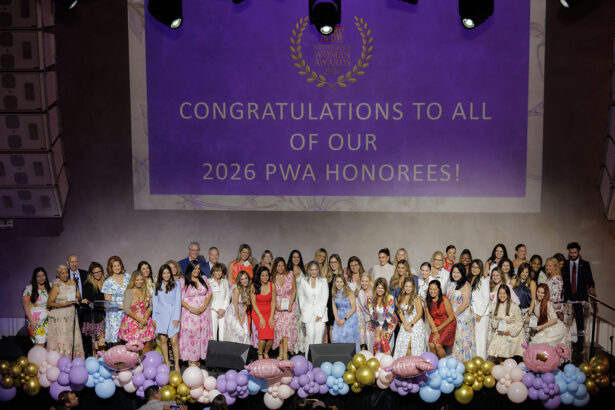 A large group of women and a few men stand on stage in front of a purple screen that reads, "Congratulations to all of our 2026 PWA Honorees!" The stage is decorated with colorful balloons and flowers. South Florida Business & Wealth