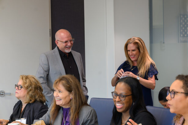 A group of six adults, both men and women, sit and stand around a conference table, smiling and interacting in a bright, modern office setting. South Florida Business & Wealth