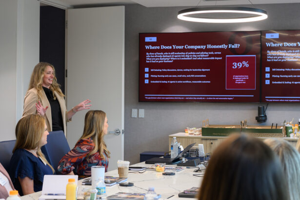 A woman stands and presents to a group in a conference room, gesturing toward a large screen displaying a slide with the title “Where Does Your Company Honestly Fall?” and a chart showing 39%. South Florida Business & Wealth