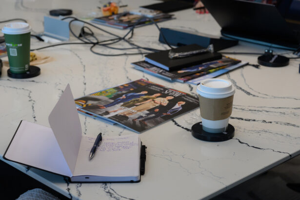 A white marble table with open notebooks, magazines, a pen, two takeaway coffee cups, laptops, and cables, suggesting an ongoing meeting or collaborative workspace. South Florida Business & Wealth