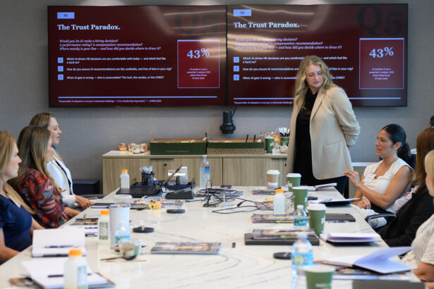 A group of women sits around a conference table in a meeting room, discussing in front of two large screens displaying a presentation titled “The Trust Paradox” with statistics and questions about building trust. South Florida Business & Wealth