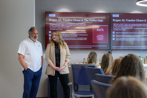 A man and a woman stand in front of a seated audience, presenting information on large screens behind them about "Rogue AI, Vendor Chaos & The Policy Gap." The screens display data and a 62% statistic. South Florida Business & Wealth