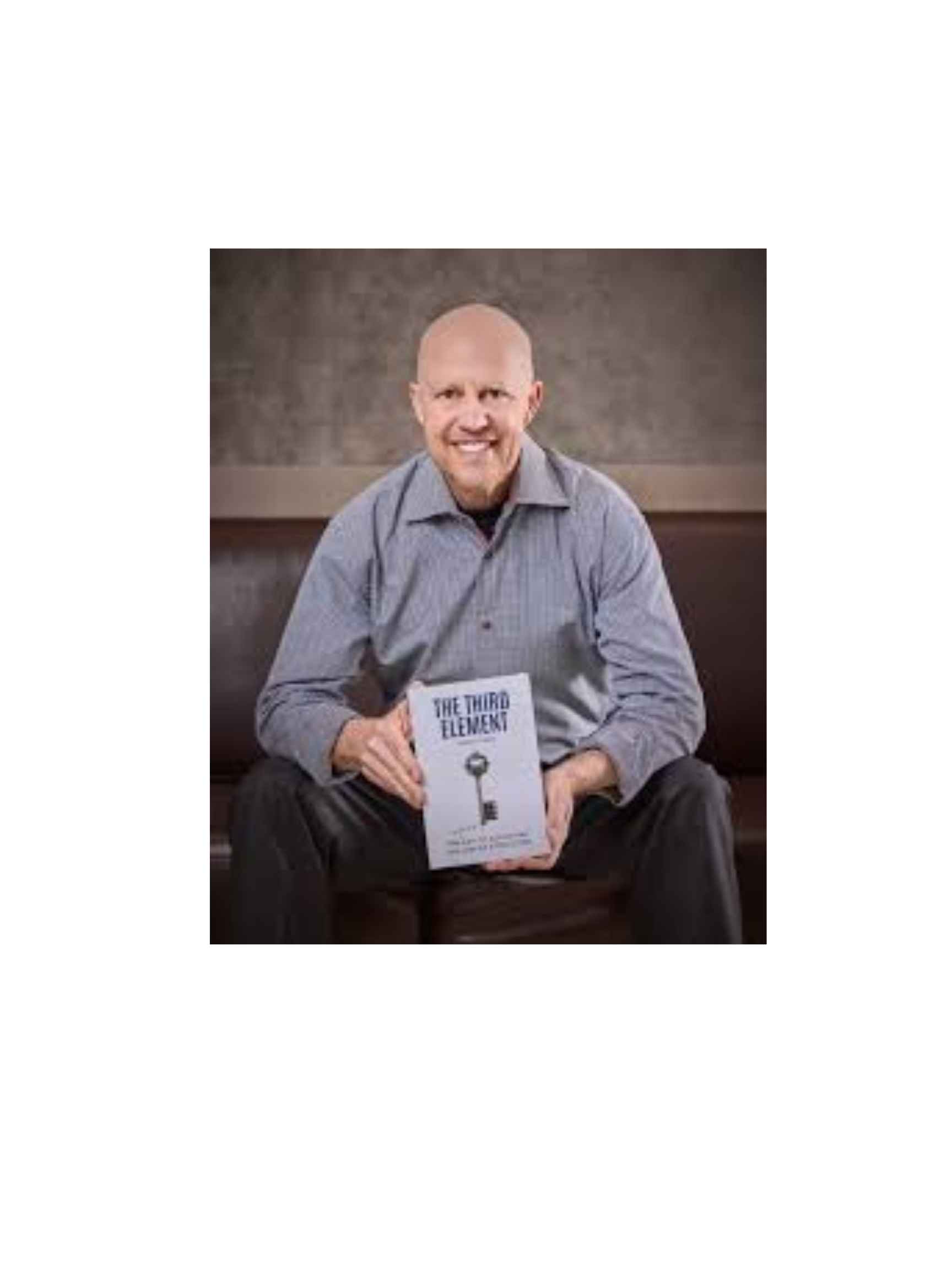 A smiling bald man in a gray shirt sits on a bench, holding a book titled "The Third Element," with a key graphic on the cover, against a neutral background. South Florida Business & Wealth