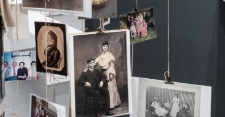 A collection of vintage and modern family photographs hangs from strings against a dark background, displaying people in various poses and outfits from different eras. South Florida Business & Wealth