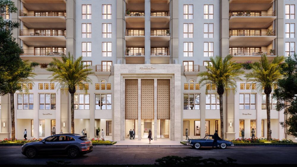 Street view of a modern, multi-story luxury apartment building with palm trees, large entrance, decorative facade, and retail shops. People walk by, and two cars are parked on the street in front of the building. South Florida Business & Wealth