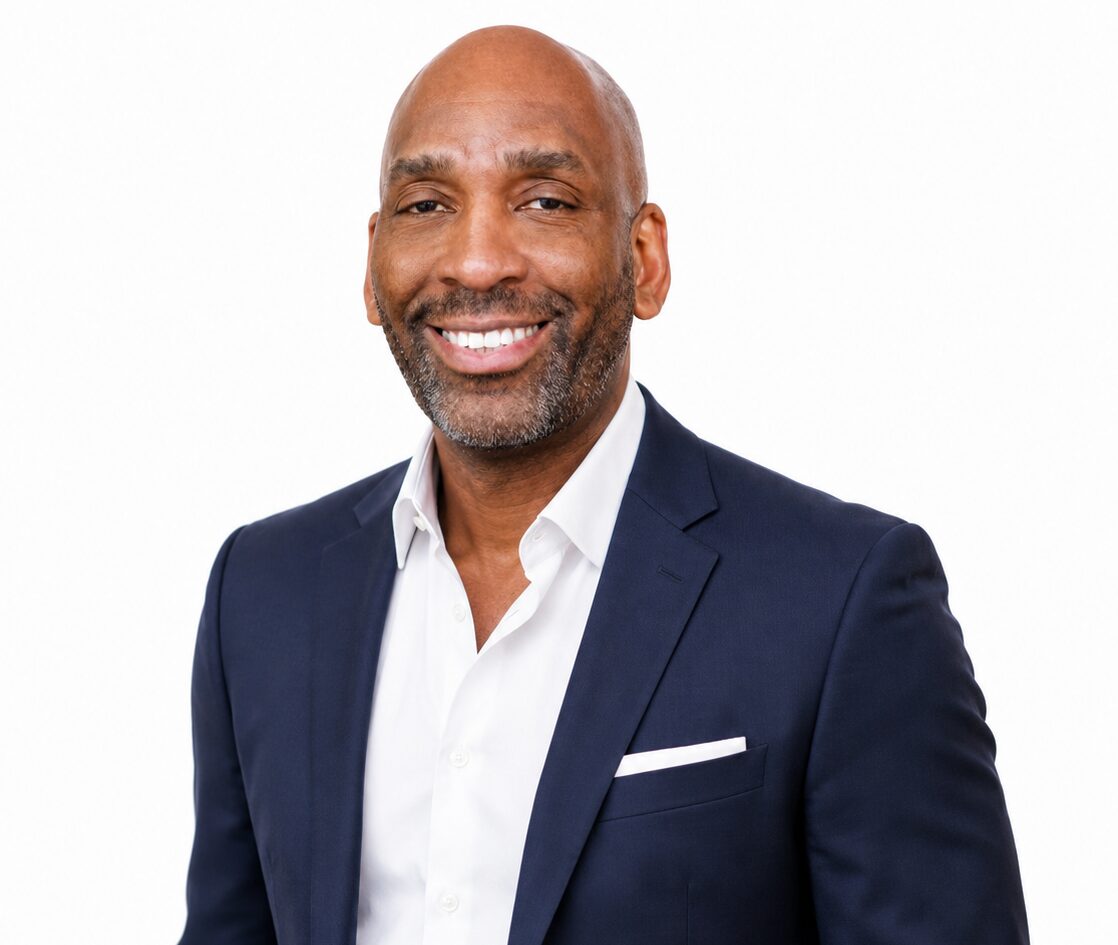 Smiling man wearing a navy blue suit jacket over a white dress shirt, standing against a plain white background. South Florida Business & Wealth