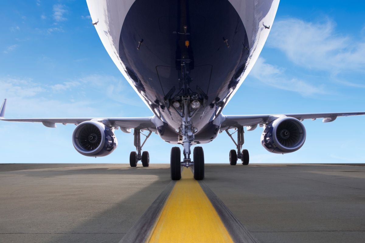 Close-up view of a commercial airplane from the front, showing its landing gear on a runway with a yellow centerline, under a clear blue sky. South Florida Business & Wealth