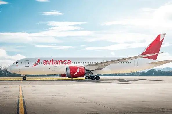 A white Avianca airplane with red accents and logo is on the runway, ready for takeoff, under a bright sky with light clouds. South Florida Business & Wealth