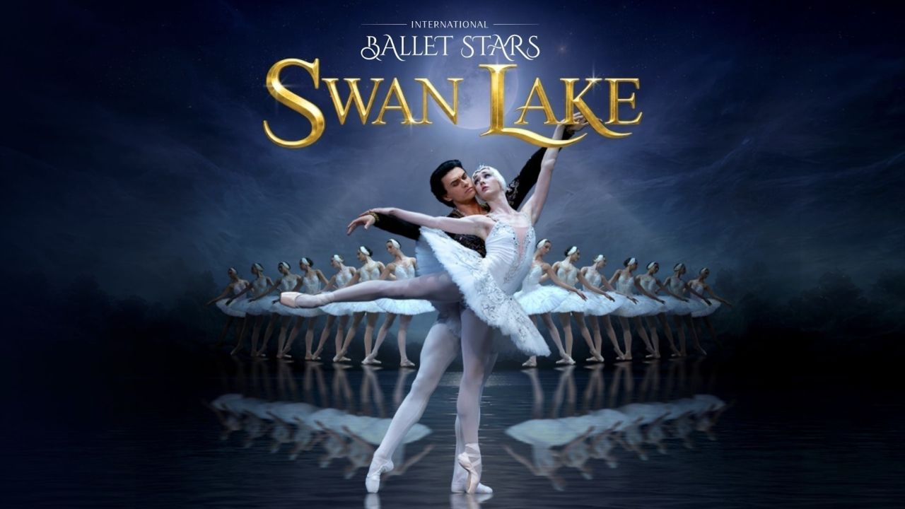 A male and female ballet dancer perform Swan Lake on stage, with ballerinas in white tutus posed behind them. The title “Swan Lake” appears in gold above them against a dark blue background. South Florida Business & Wealth