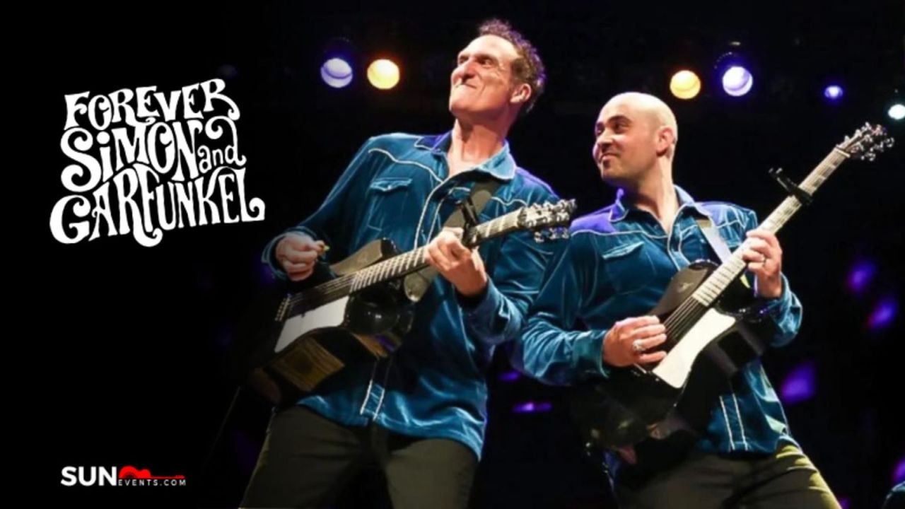 Two musicians in matching blue shirts play guitars on stage under colorful lights. “Forever Simon and Garfunkel” is written in white stylized text on the left. The SUN Events logo appears in the bottom left corner. South Florida Business & Wealth