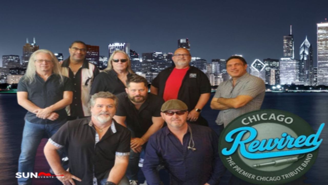 Eight men pose in front of a nighttime Chicago skyline backdrop. A circular logo in the foreground reads “Chicago Rewired: The Premier Chicago Tribute Band.”. South Florida Business & Wealth
