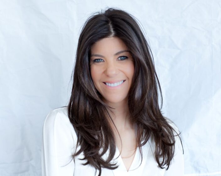 Woman with long dark hair and light skin smiles at the camera, wearing a white top, with a plain white background behind her. South Florida Business & Wealth