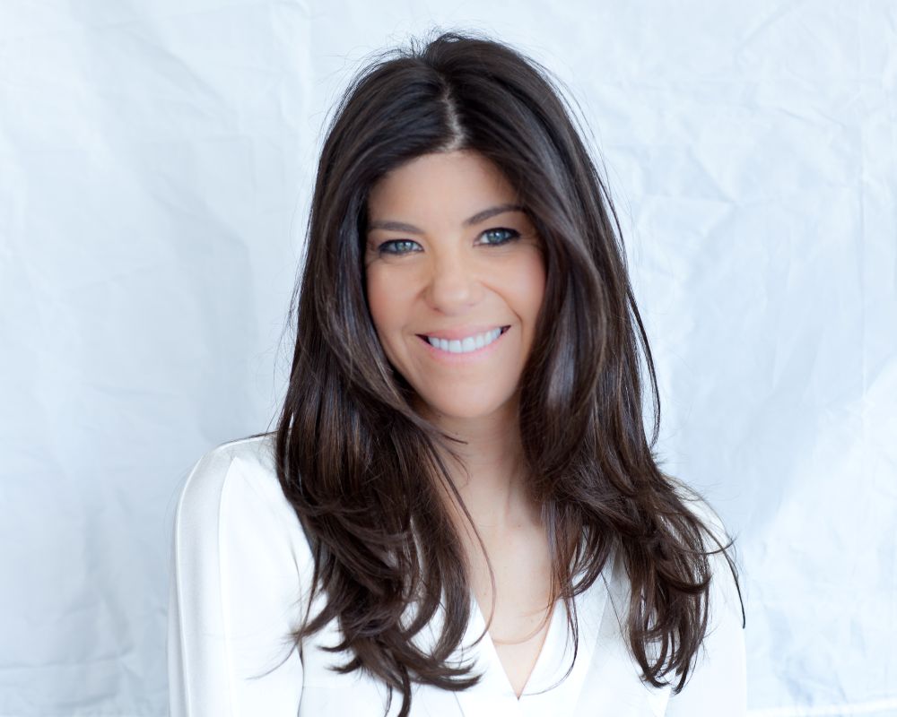 Woman with long dark hair and light skin smiles at the camera, wearing a white top, with a plain white background behind her. South Florida Business & Wealth