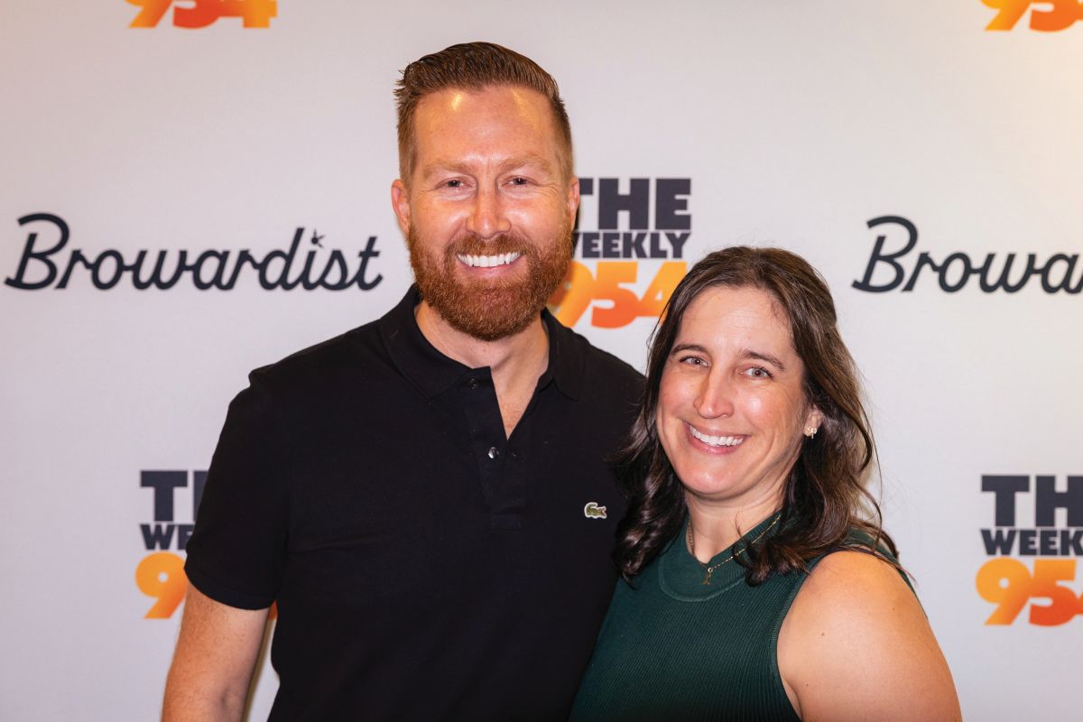 A man and woman smile together in front of a step-and-repeat backdrop with logos reading “Browardist” and “THE WEEKLY 954”. South Florida Business & Wealth