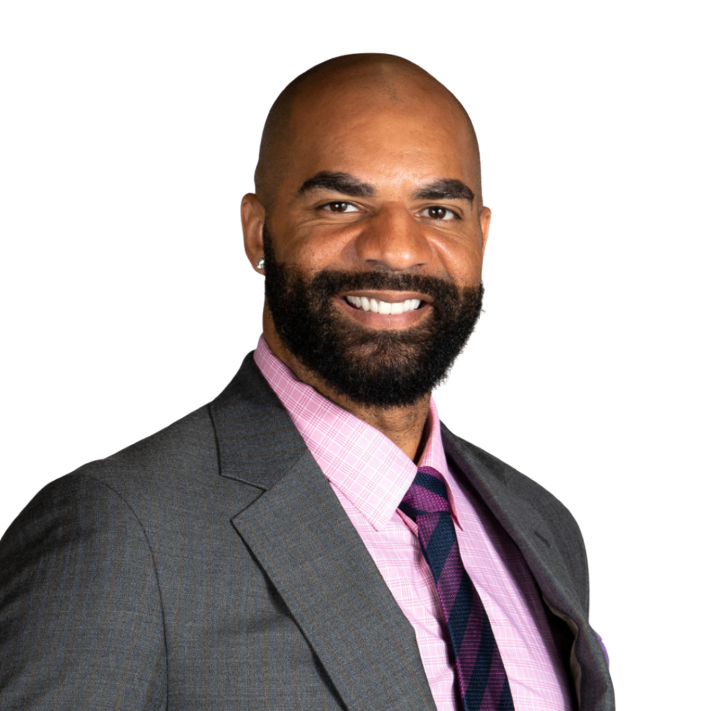 A smiling man with a shaved head and a beard, wearing a gray suit, pink patterned shirt, and a dark necktie. South Florida Business & Wealth